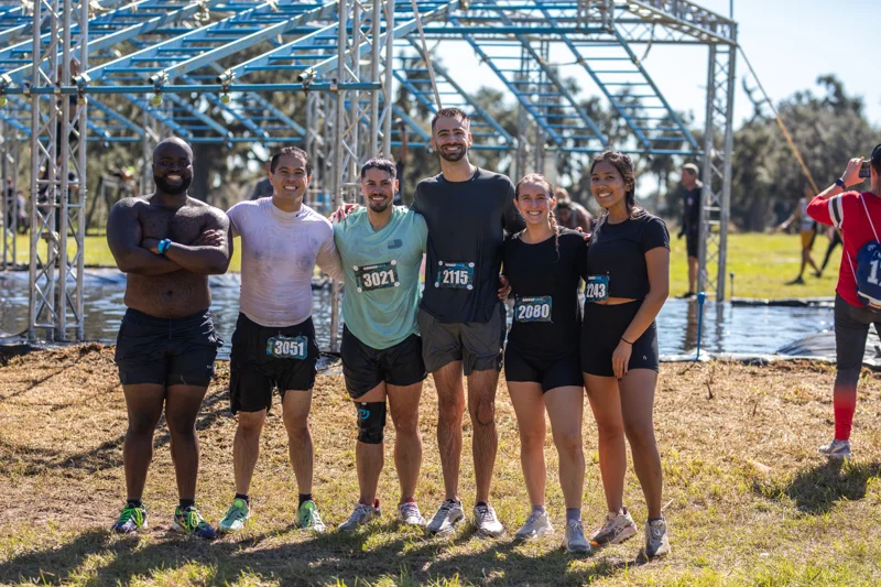 Six friends smile together beside the obstacle course