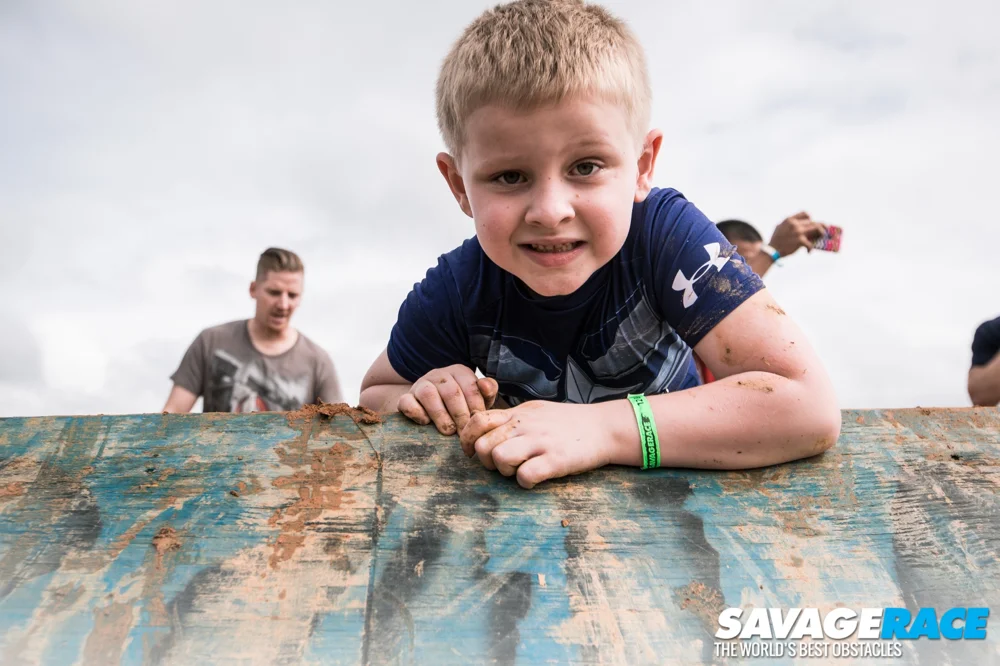 A young SavageJR racer smiles as he climbs over a wooden obstacle