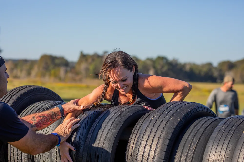 A smiling racer accepts a helping hand over a tire obstacle